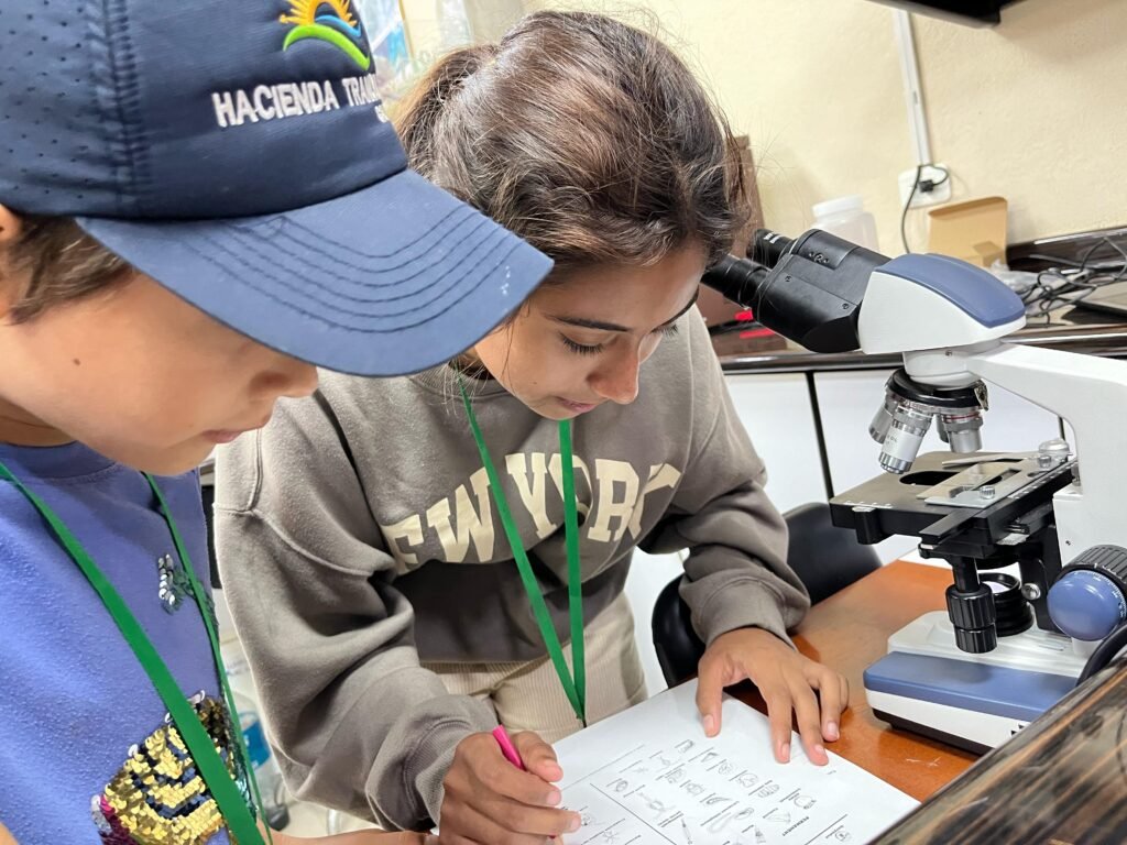 two children next to a microscope making notes on paper